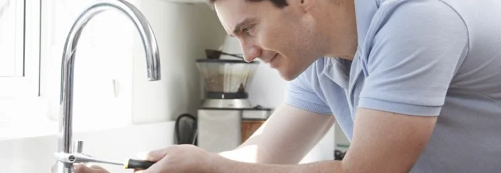 Person repariert Wasserhahn mit Schraubenzieher.