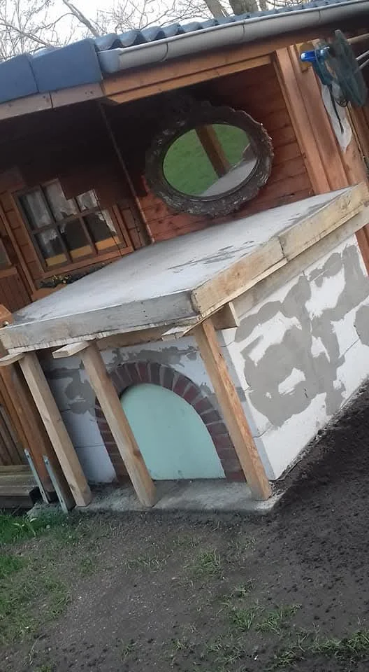 Ein im Bau befindlicher, gemauerter Ofen vor einer Holzhütte im Garten.