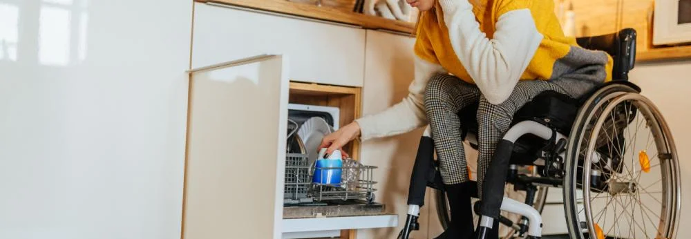Frau im Rollstuhl benutzt Geschirrspüler.