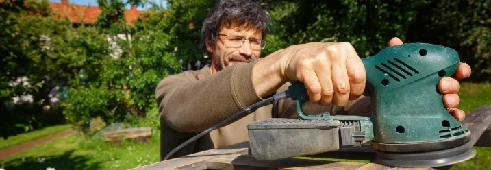 Person schleift Gartenmöbel ab