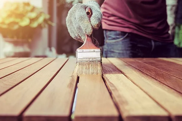 Person streicht Holztisch mit Pinsel