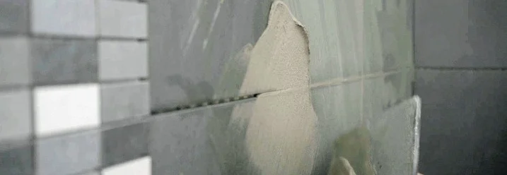 Person verfugt dunkle Wandfliesen.