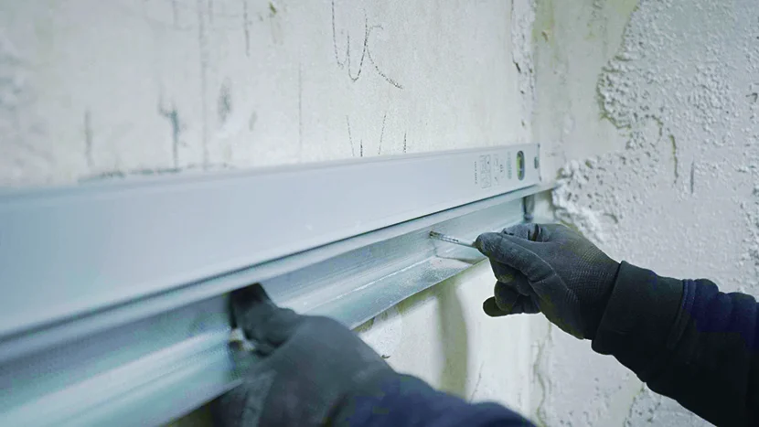 Person montiert eine Metallschiene an eine Wand.