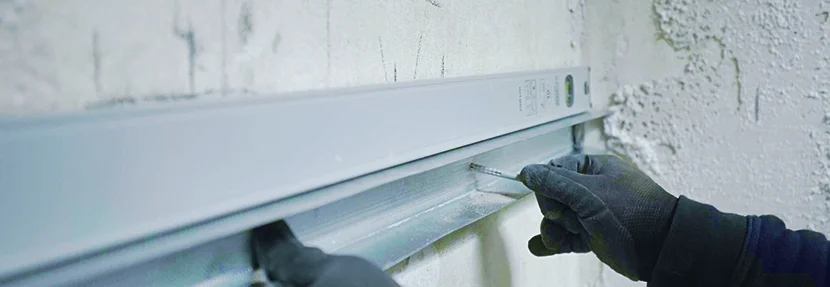 Person montiert eine Metallschiene an eine Wand.