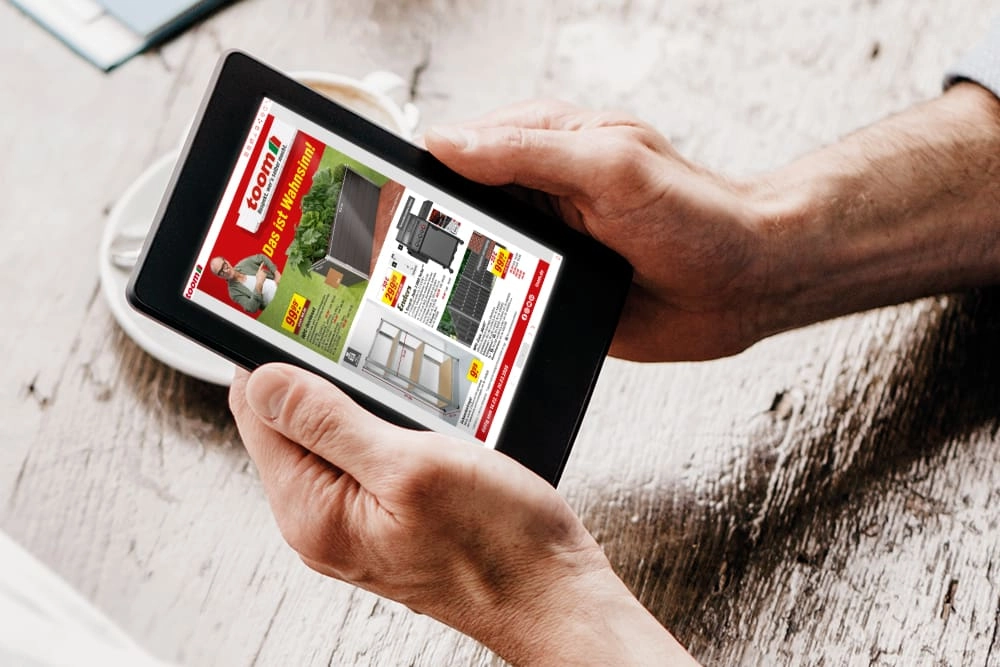 Hände halten ein Tablet, auf dem ein digitaler Prospekt zu sehen ist.