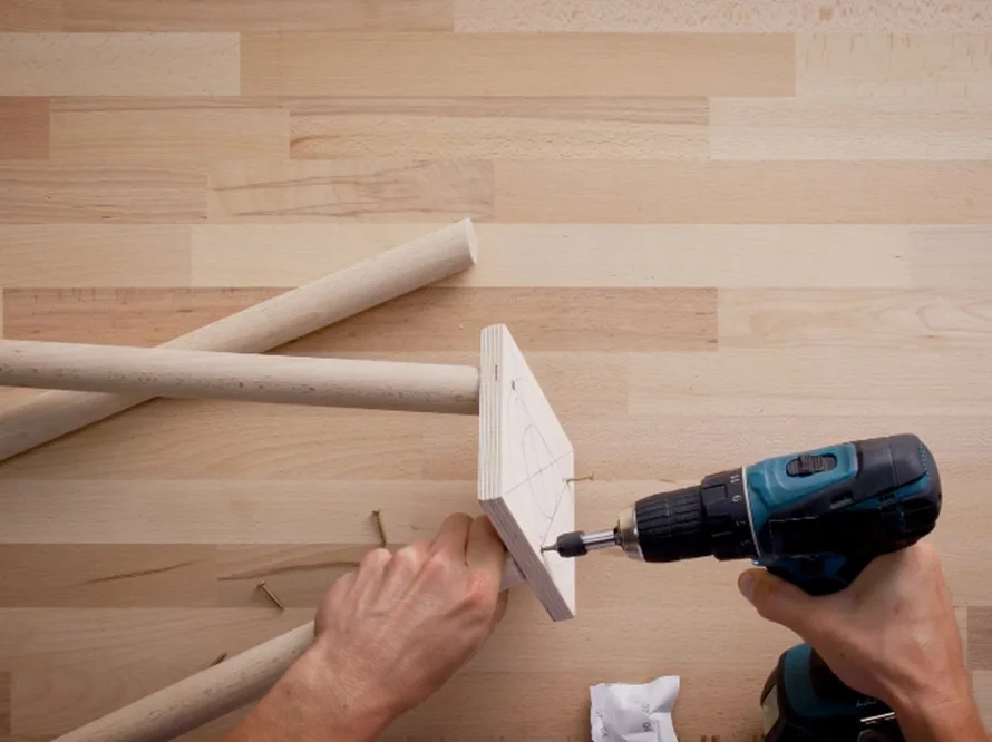 Person verschraubt Holzbeine mit Akkuschrauber an Holzplatte