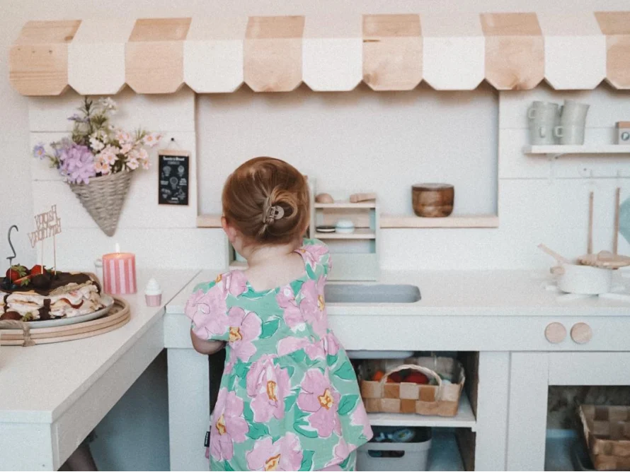 Kind von hinten an einer weißen Spielküche.