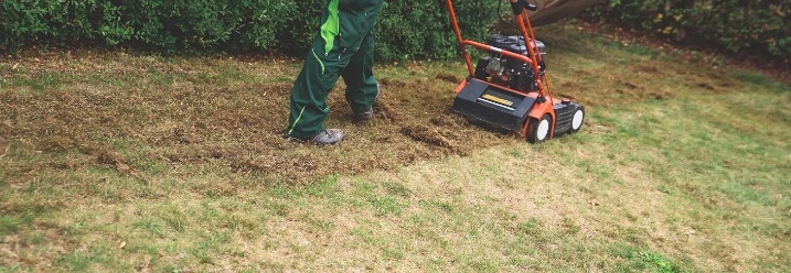 Person vertikutiert Rasen