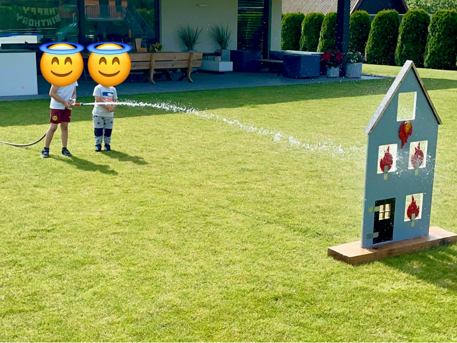 Zwei Kinder löschen mit Gartenschlauch Spielzeughaus