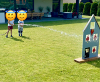 Zwei Kinder löschen mit Gartenschlauch Spielzeughaus