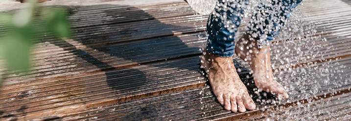 Person gießt Holzterrasse mit Gießkanne