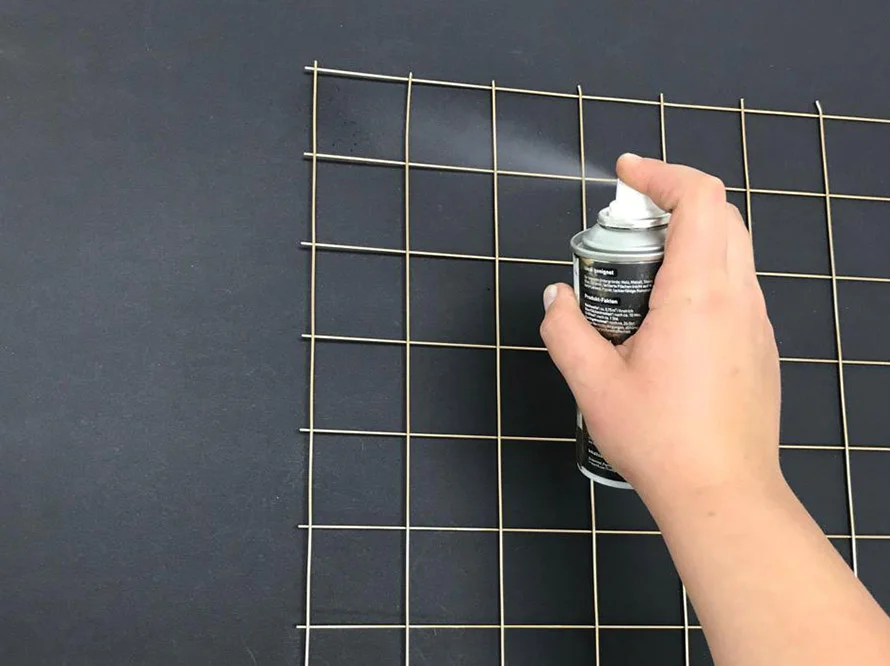 Person sprüht Farbe auf ein Metallgitter.