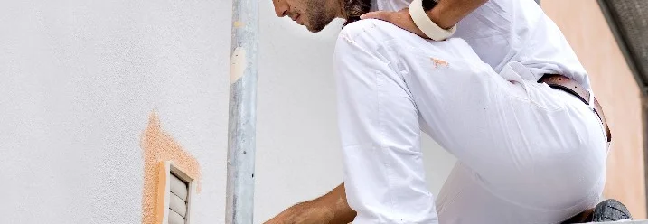 Person auf Gerüst streicht Hauswand