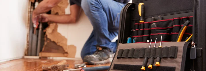 Werkzeugkiste im Vordergrund, Person repariert Wand im Hintergrund
