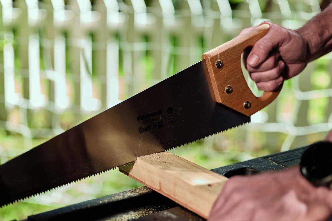 Eine Person sägt mit einer Handsäge ein Stück Holz durch.