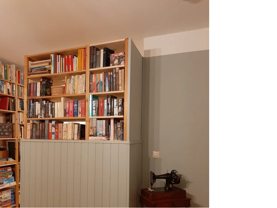 Ein Bücherregal mit einer Nähmaschine daneben.