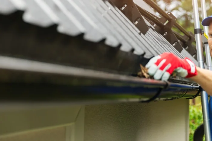 Person reinigt Dachrinne