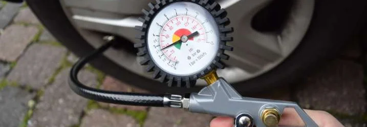 Person prüft Reifendruck mit Manometer