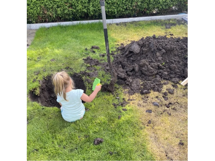 Kind mit Schaufel gräbt Loch in Wiese