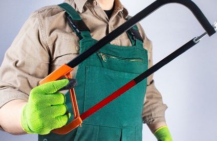 Metallsäge Arbeiters in grünem Overall mit Schutzhandschuhen und einer Bügelsäge