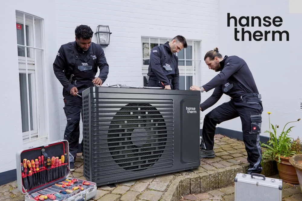 Drei Personen installieren eine Wärmepumpe. Das Logo der Marke hansetherm ist abgebildet.