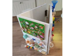 Ein weißes Spielhaus aus Holz mit verschiedenen motorischen Aktivitäten darauf.