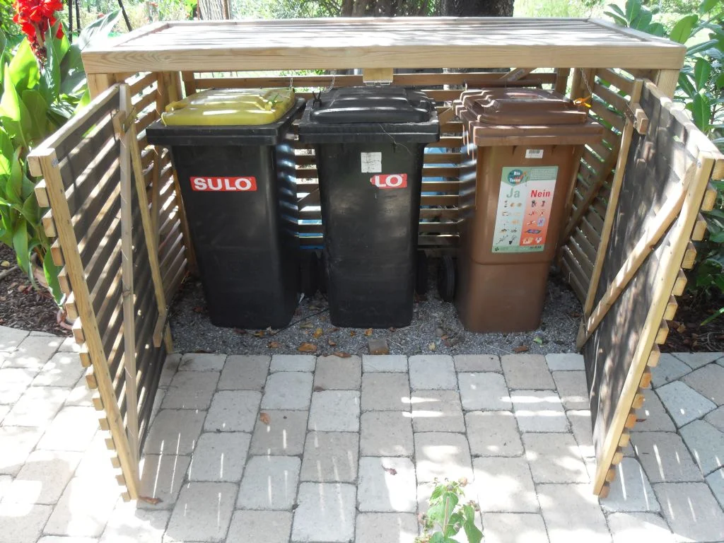 Holzterrasse mit drei Mülltonnen in einem Unterstand
