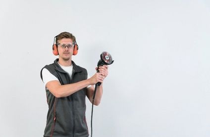Natursteinfliesen schneiden Handwerker mit Schutzbrille und Gehörschutz hält einen Winkelschleifer in der Hand.