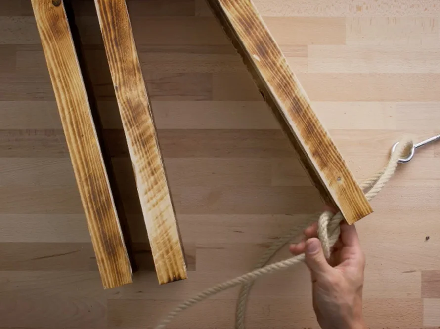 Hand befestigt Seil an Holzlatten.