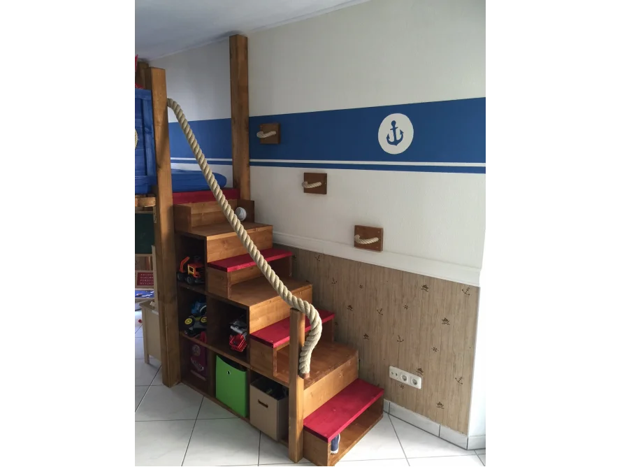 Holztreppe mit rotem Geländer zu einem Hochbett