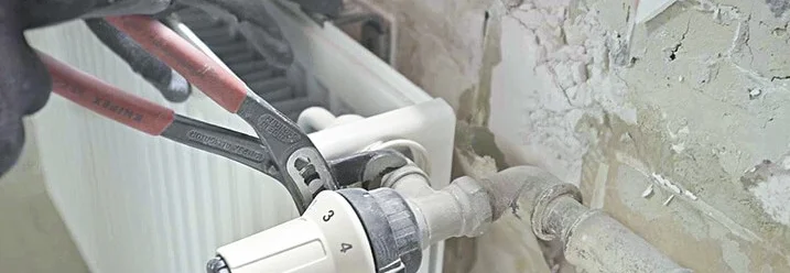 Person montiert Heizkörper mit Rohrzange ab.