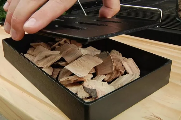 Hand öffnet Räucherbox mit Holzchips