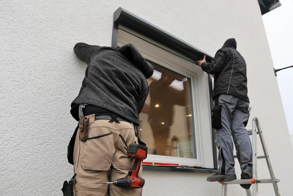 Zwei Personen montieren einen Rollladen an einem Fenster.