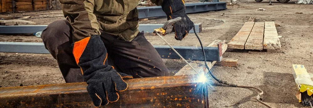 Person schweißt Metallträger auf Baustelle.