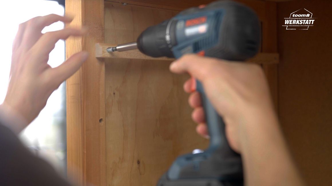 Person schraubt Holzbrett mit Akkuschrauber fest