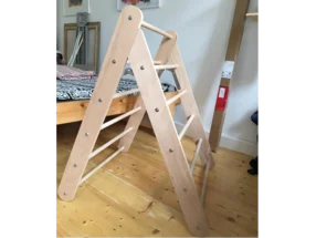 Ein Kletterdreieck aus Holz steht auf einem Holzboden in einem Zimmer.