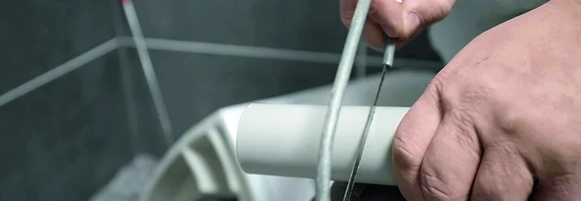 Person kürzt Rohr mit Säge.