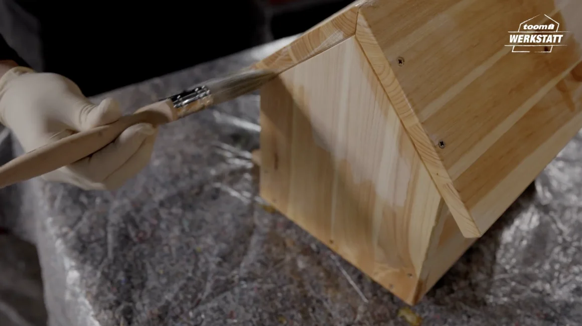 Person streicht Holzhaus mit Pinsel