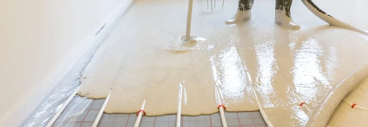 Person gießt Estrich auf Fußbodenheizung.