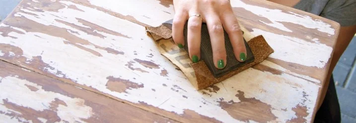 Person schleift Holztisch mit Schleifpapier