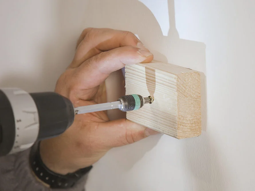 Hand befestigt Holz mit Akkuschrauber an Wand