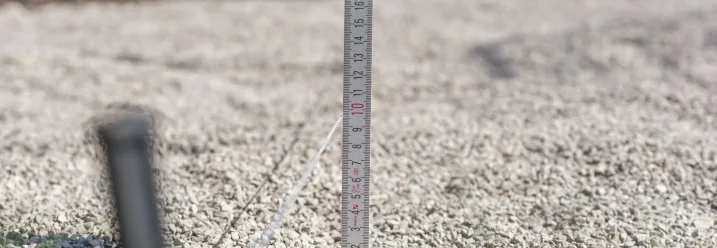 Ein Zollstock steckt in einer Schicht Kies.