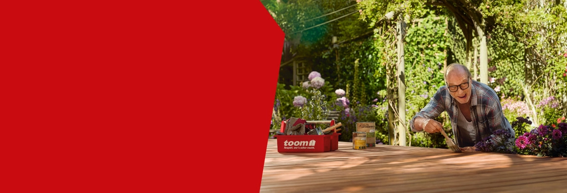 Mensch streicht mit einem Pinsel eine Holzterrasse im Garten.