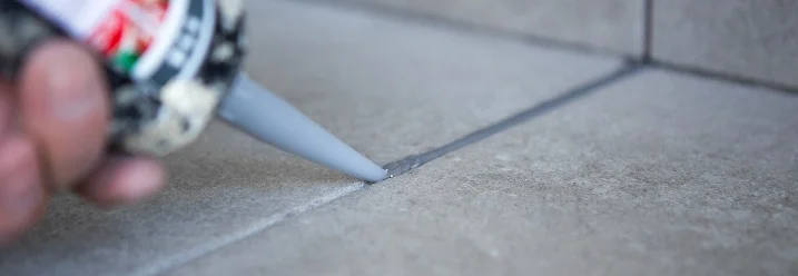 Hand trägt Dichtungsmasse auf Fliesen auf