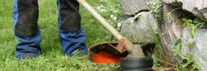 Person trimmt Rasen mit Rasentrimmer