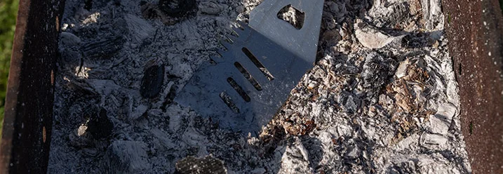 Graue Asche in einem Grill mit einem Grillwender