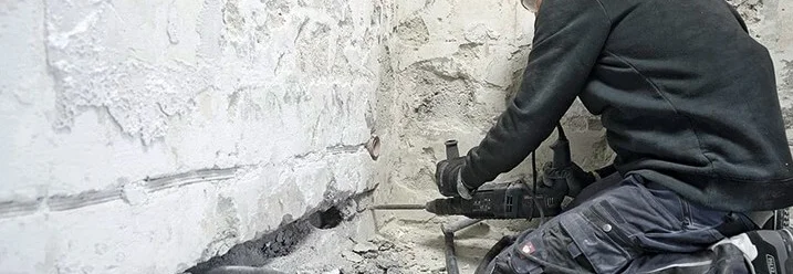 Person mit Bohrhammer an Wand