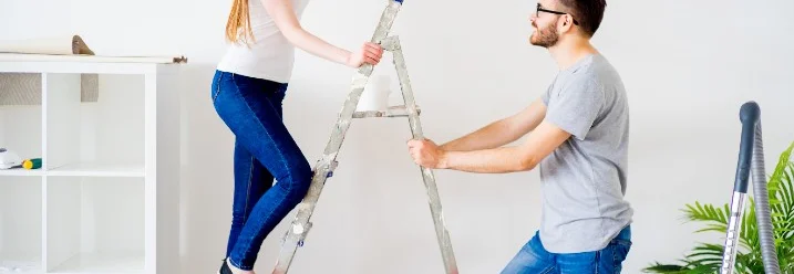 Person auf Leiter reicht Gegenstand an zweite Person