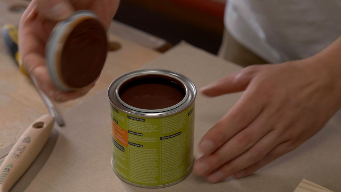 Person öffnet Dose mit brauner Farbe