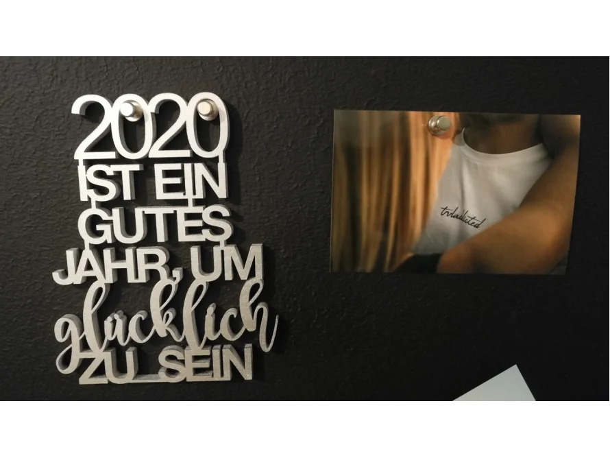 Silberner Schriftzug "2020 ist ein gutes Jahr, um glücklich zu sein" und Foto einer Umarmung an schwarzer Pinnwand
